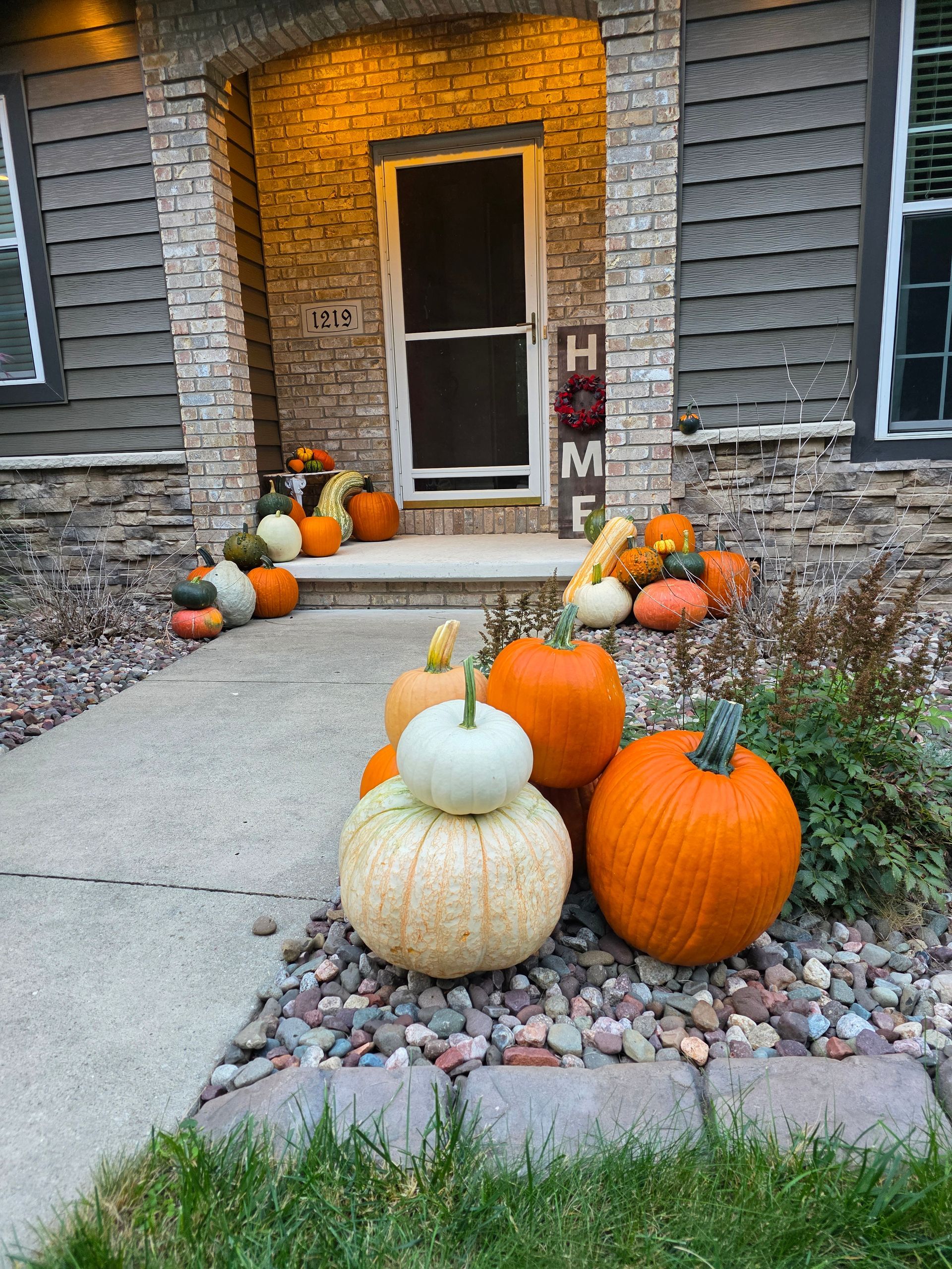 Fall-decorated home entrance with pumpkins of various colors and sizes arranged near the door and along the walkway.
