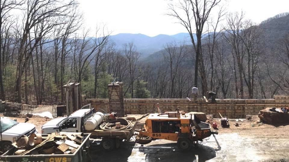 Construction site with stone wall, vehicles, equipment, and mountain backdrop.