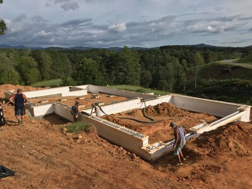 Construction site: White foundation walls, dirt, men working; scenic, hilly background.