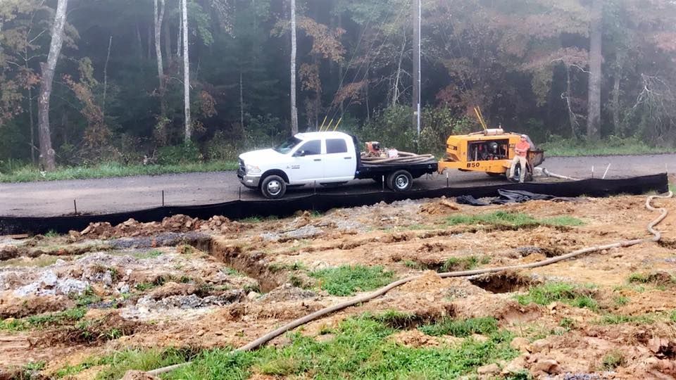 A white work truck and yellow generator on a road undergoing construction, with trenches in the foreground.