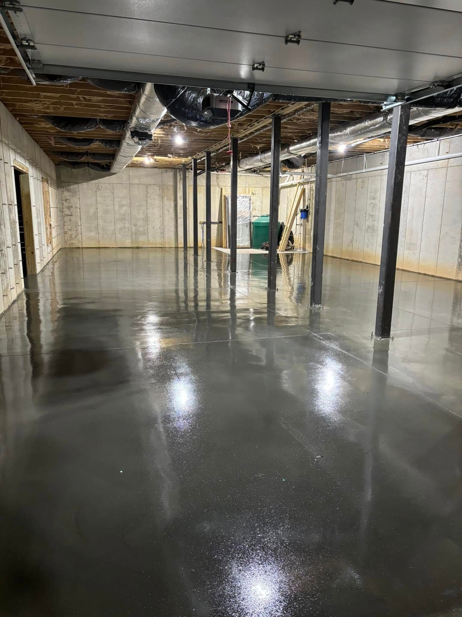 Gray concrete floor in a basement with support beams and ductwork.