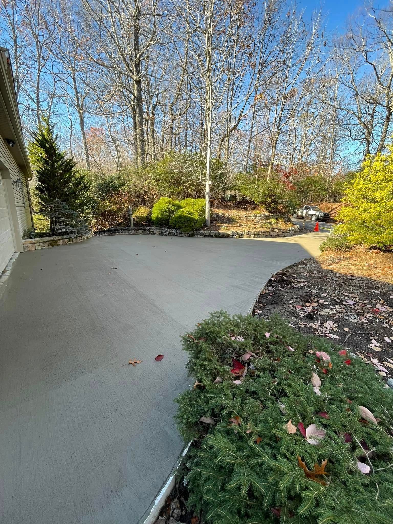Concrete patio next to a building, bordered by bushes and trees.