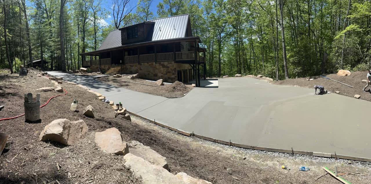 A cabin in a wooded area with a newly poured concrete driveway.