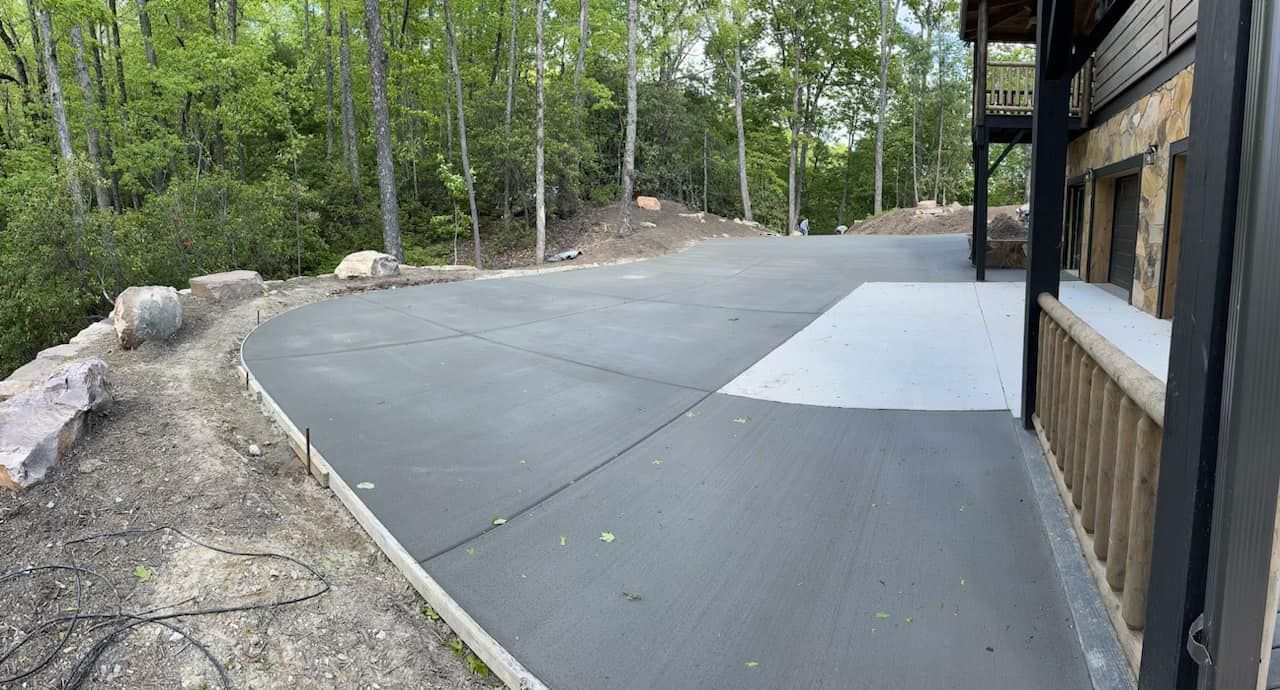 Asphalt driveway next to a log cabin, curving uphill, trees in background.
