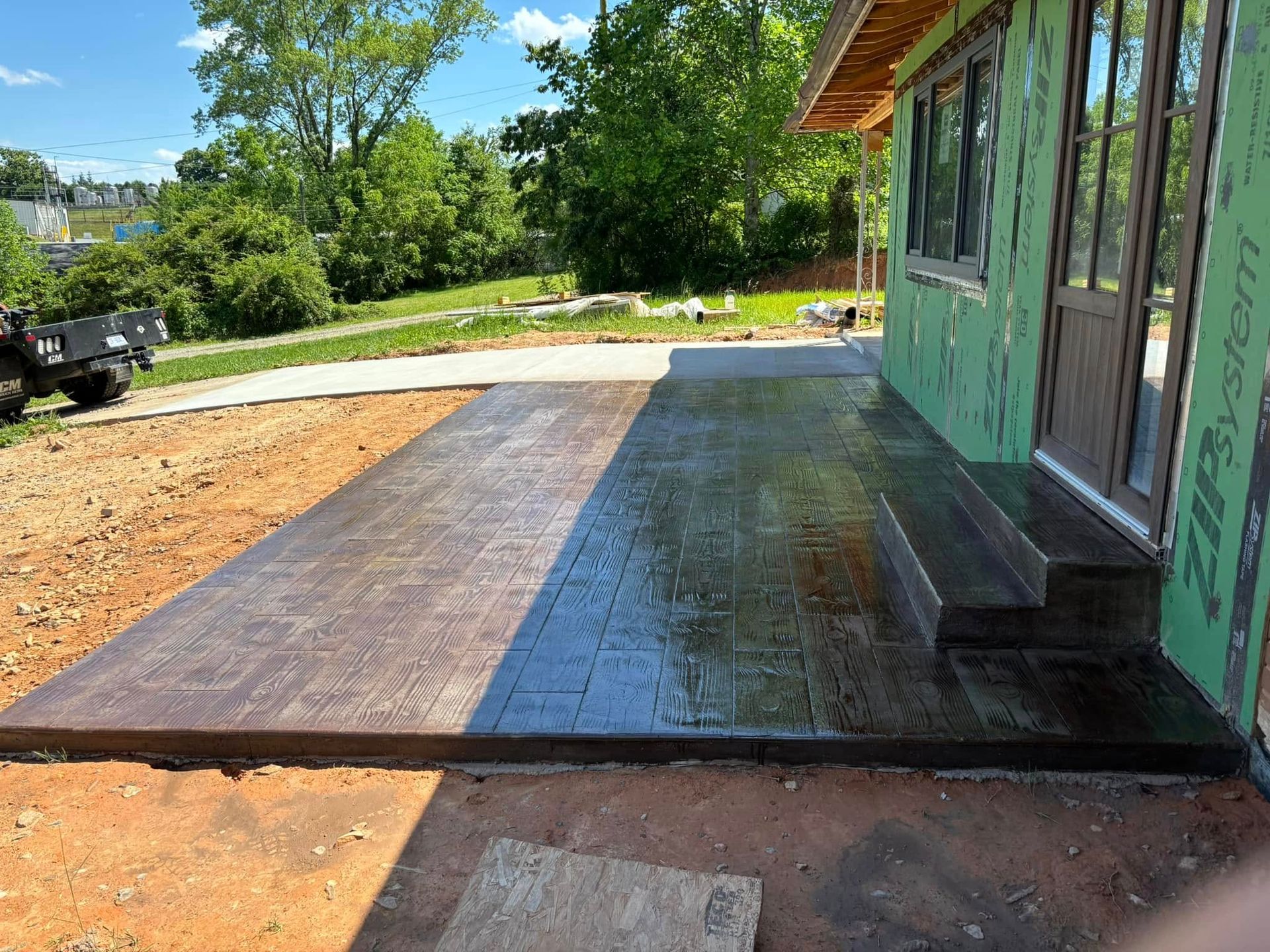Newly poured concrete patio with steps next to a house under construction.
