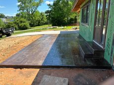 Newly poured concrete patio with steps next to a house under construction.