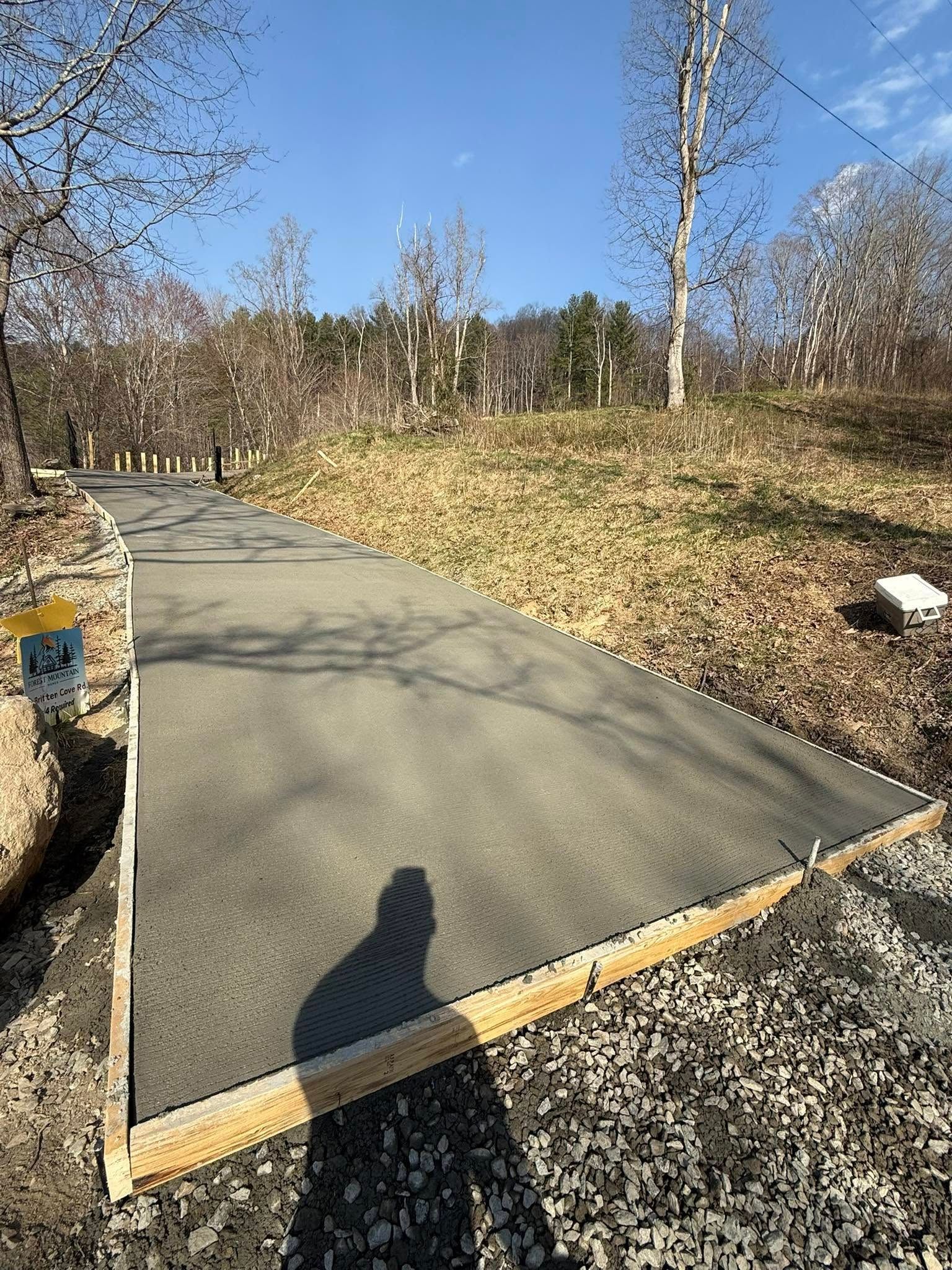Asphalt walkway with wooden edging, leading uphill into a grassy area with trees and blue sky.