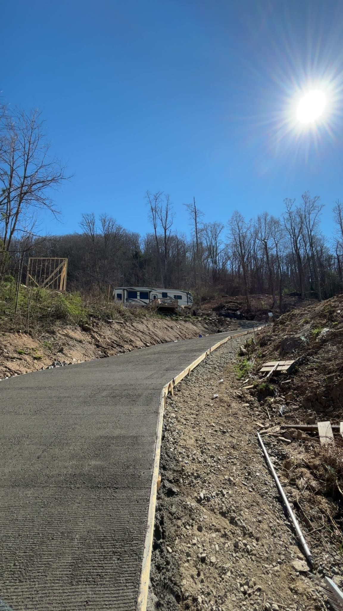 Gravel path winding uphill with retaining walls, leading to a mobile home on a sunny day.