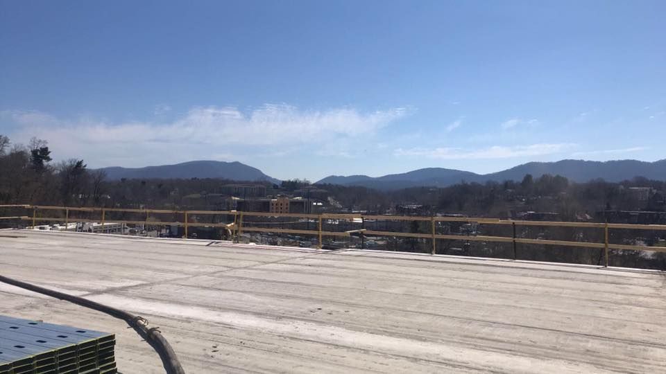 Construction site with a white surface and yellow railing, with mountains and sky in the background.