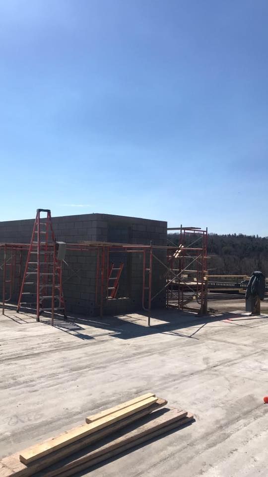 Construction site with brick walls and scaffolding under a blue sky. A ladder stands nearby.