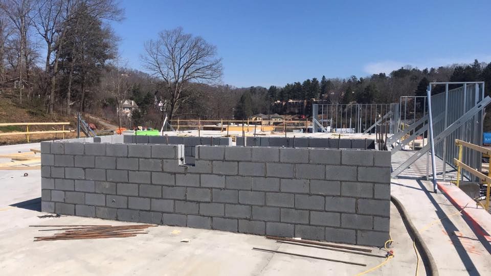 Construction site with cinder block walls and metal framing, outdoors on a sunny day.