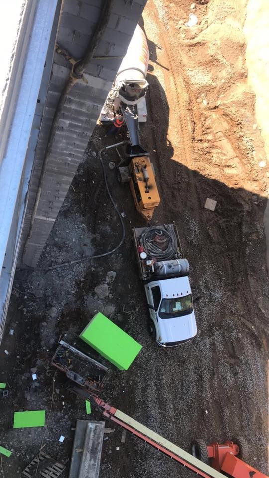Construction site with machinery under a concrete bridge. White truck, yellow drill, concrete mixer, dirt and bright green foam.