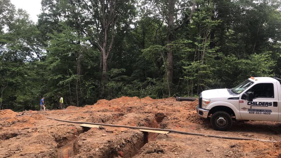 Construction site with white truck, trench, and trees in background.