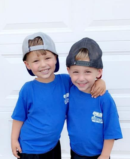 Two young boys in blue shirts and caps, smiling, one with an arm around the other.