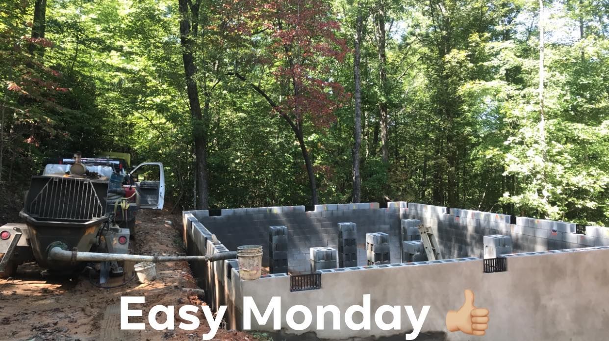 Construction site with a concrete foundation, a truck, and a wooded background. 