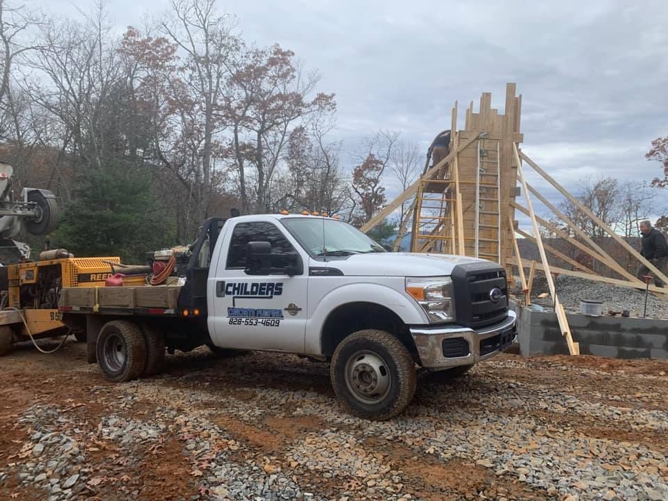 White work truck with company logo parked at a construction site with wooden framework and a cloudy sky.