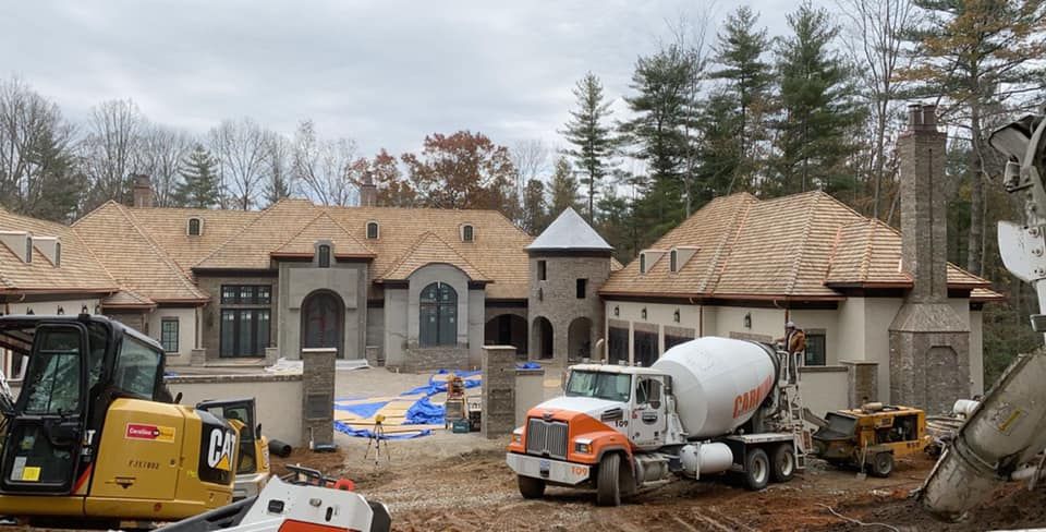 Construction site with large house, concrete truck, and heavy machinery; overcast day.
