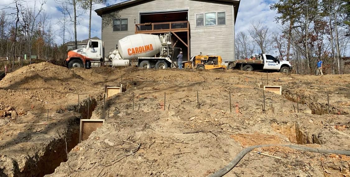 Construction site with cement truck pouring concrete into foundation forms. Building in background.