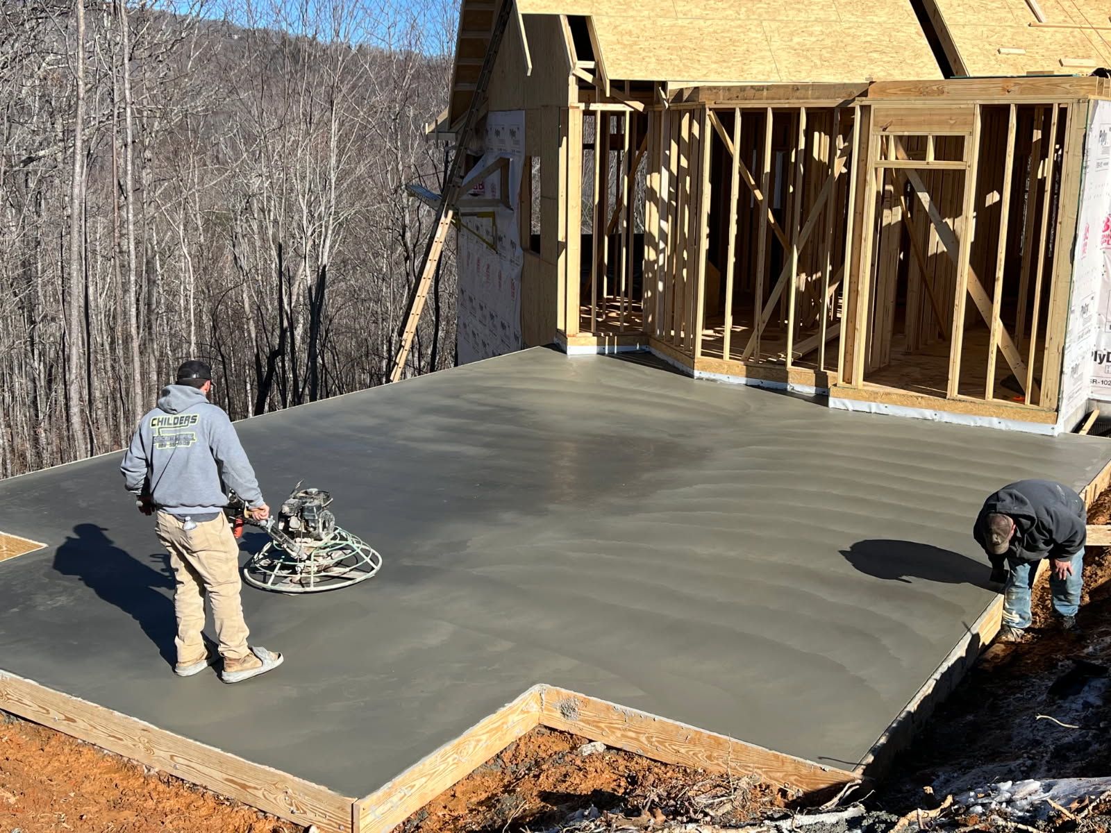 Workers smoothing wet concrete on a patio with a power trowel, framing visible.