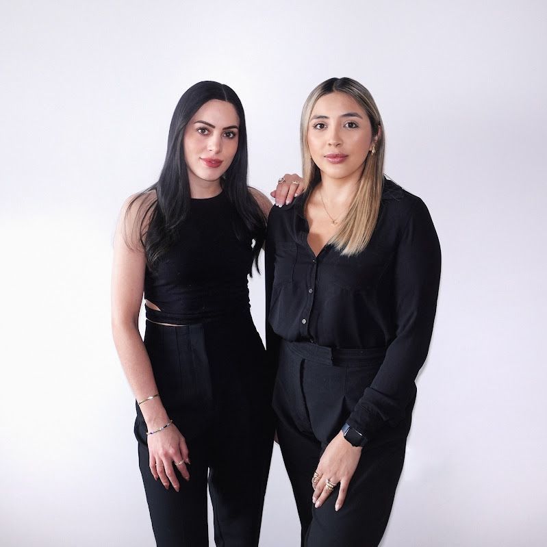 Two women in black outfits standing against a light studio backdrop