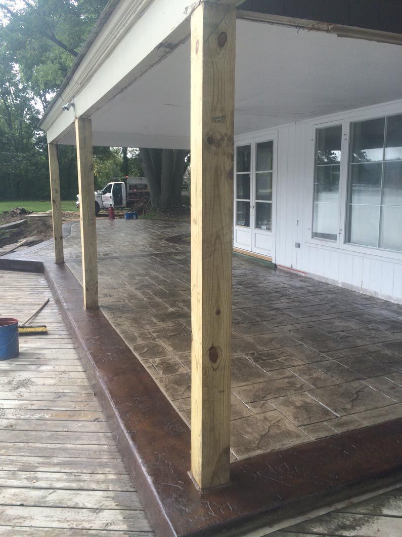 A covered patio with wooden pillars and a white house in the background.