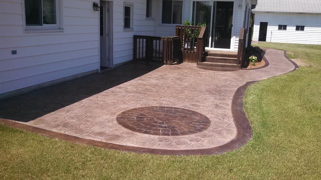 A patio with a circular design on it is in the backyard of a house.