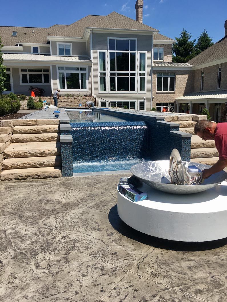 A man is working on a fountain in front of a large house.