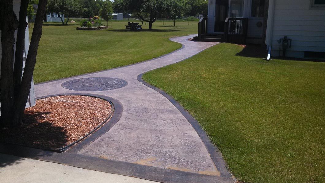 A concrete walkway leading to a house with a lush green lawn.