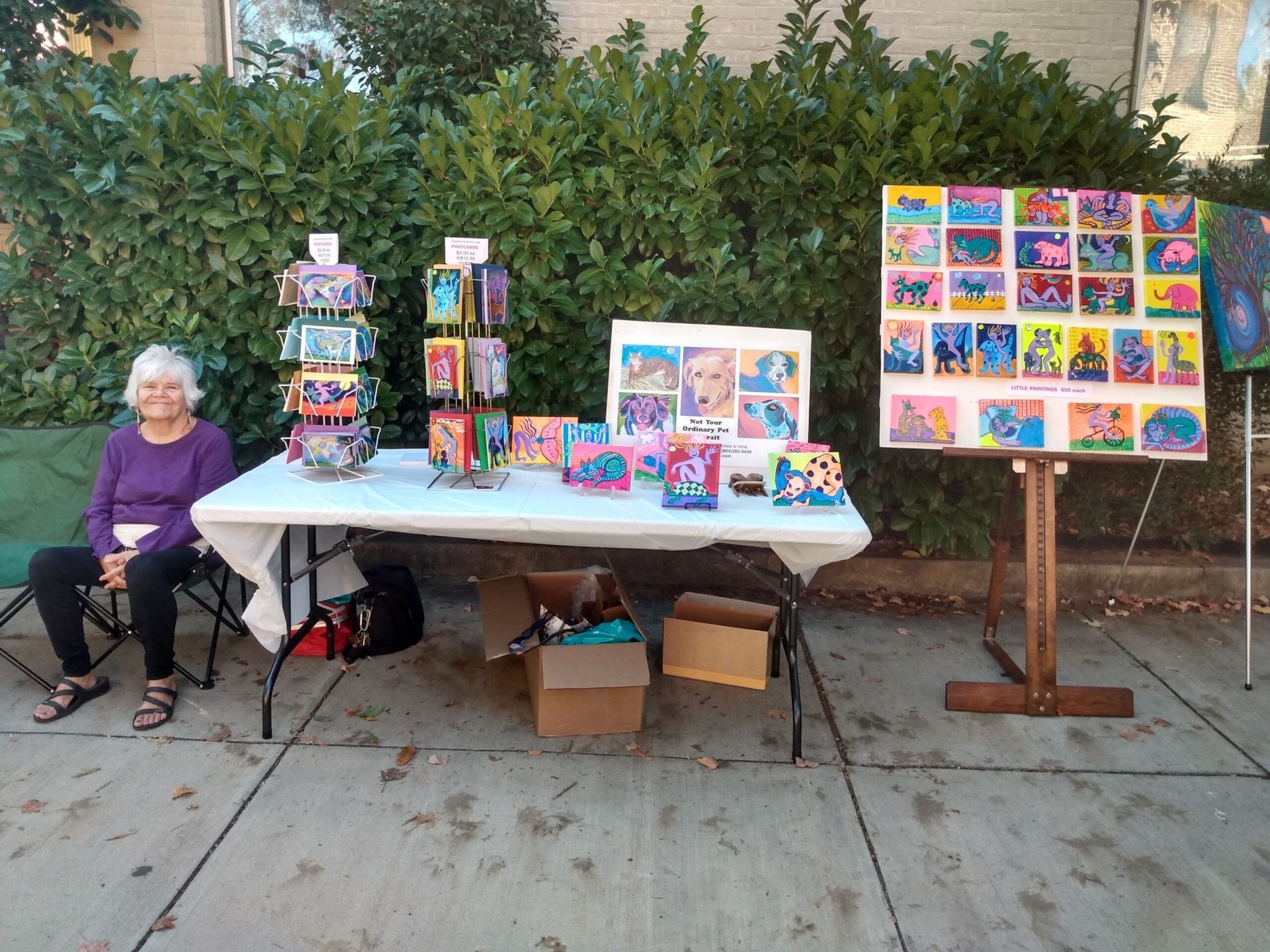 Woman at art market display of colorful art cards and paintings outdoors.
