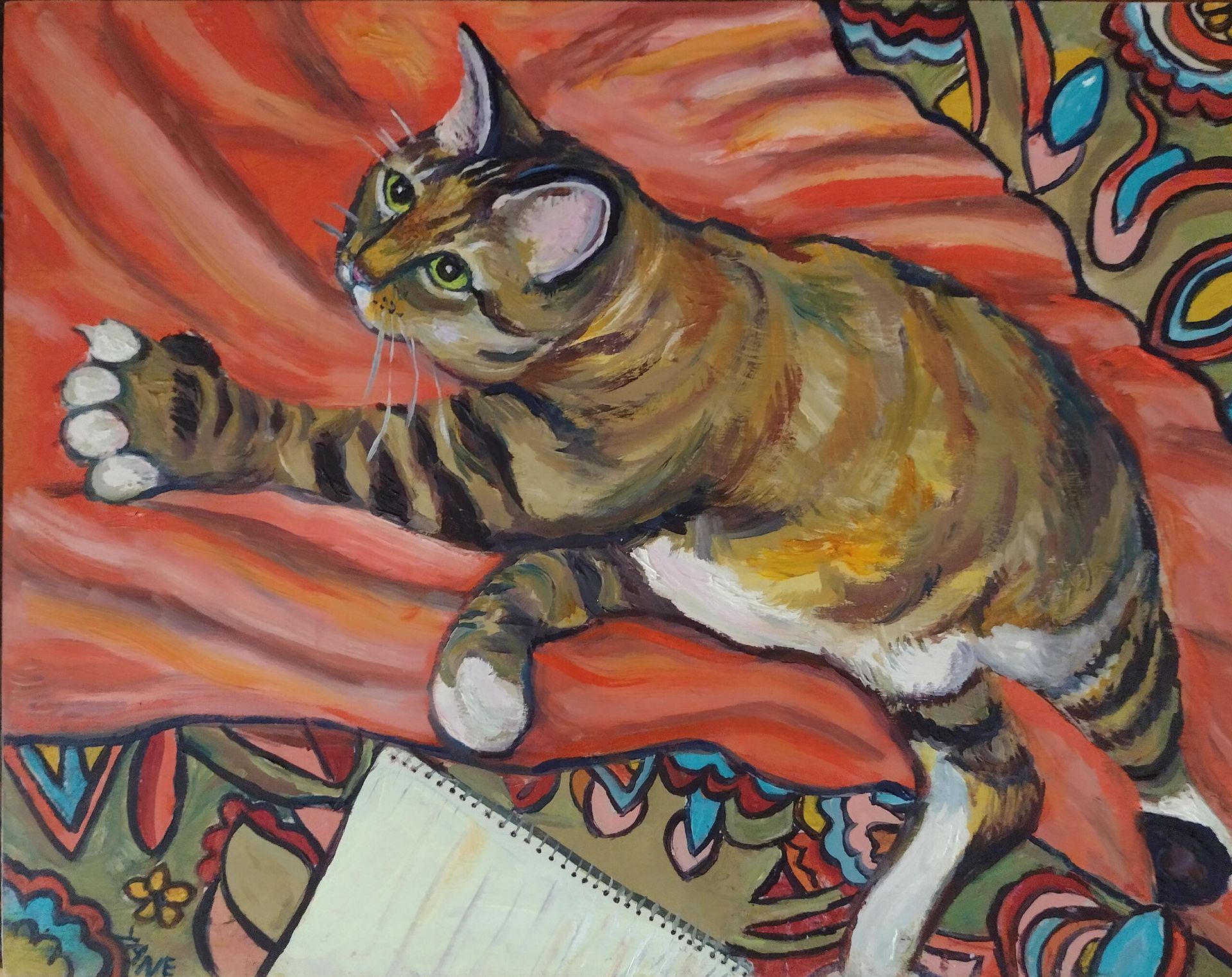 Brown tabby cat reaching towards a notebook on a paisley print surface.