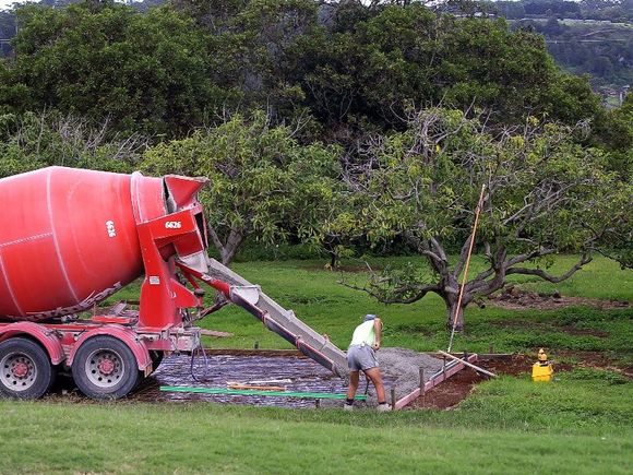 A red concrete mixer is pouring concrete into a hole