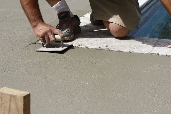 A man is kneeling down and using a trowel on a concrete surface.