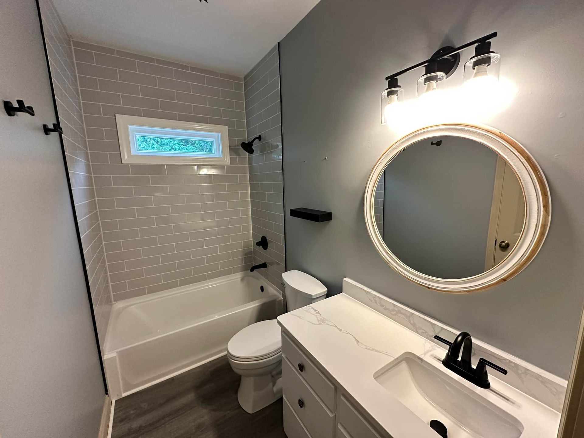 Bathroom with gray tile and walls, white vanity, round mirror, and black fixtures.