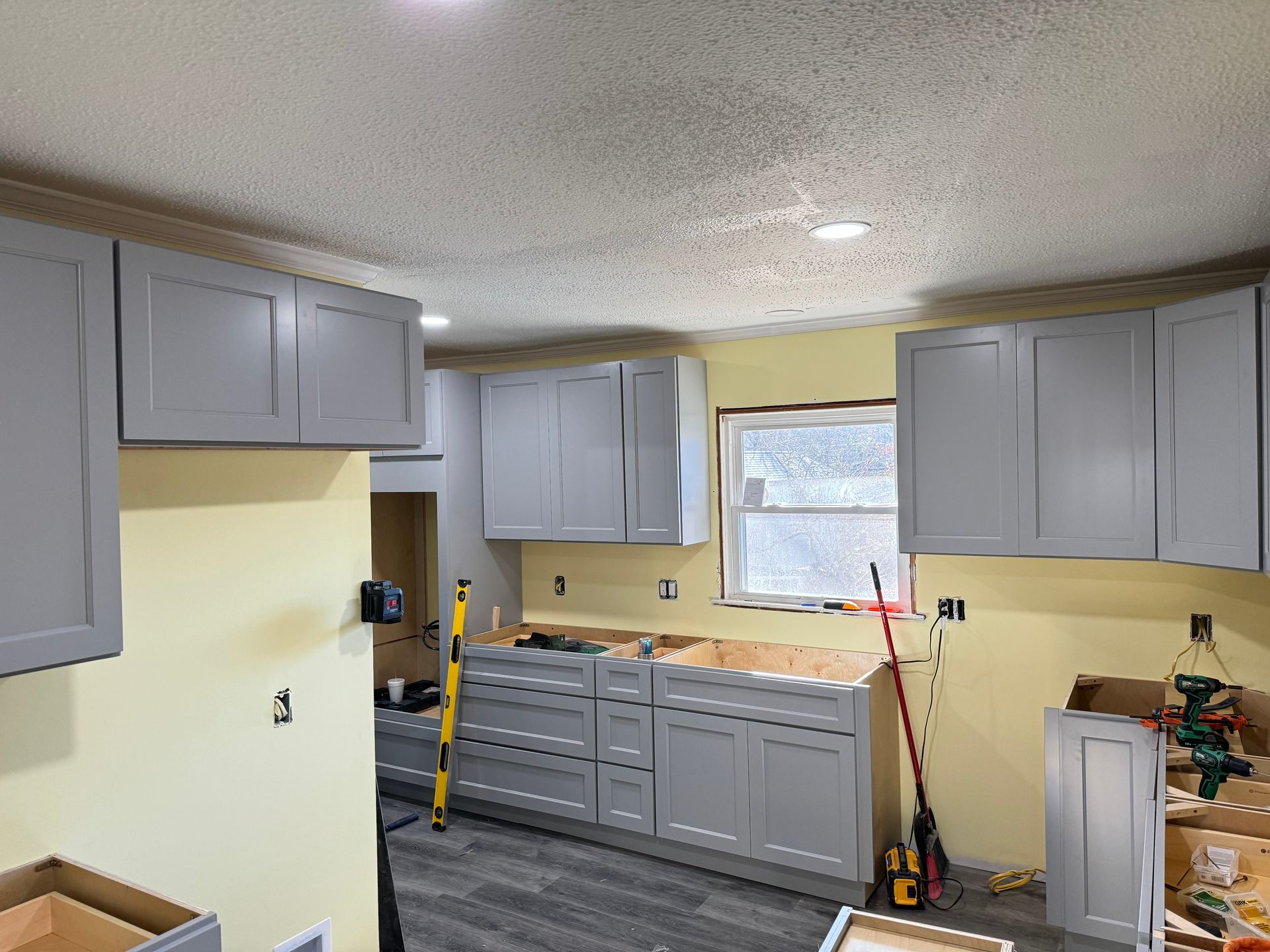 Gray kitchen cabinets being installed against light yellow walls.