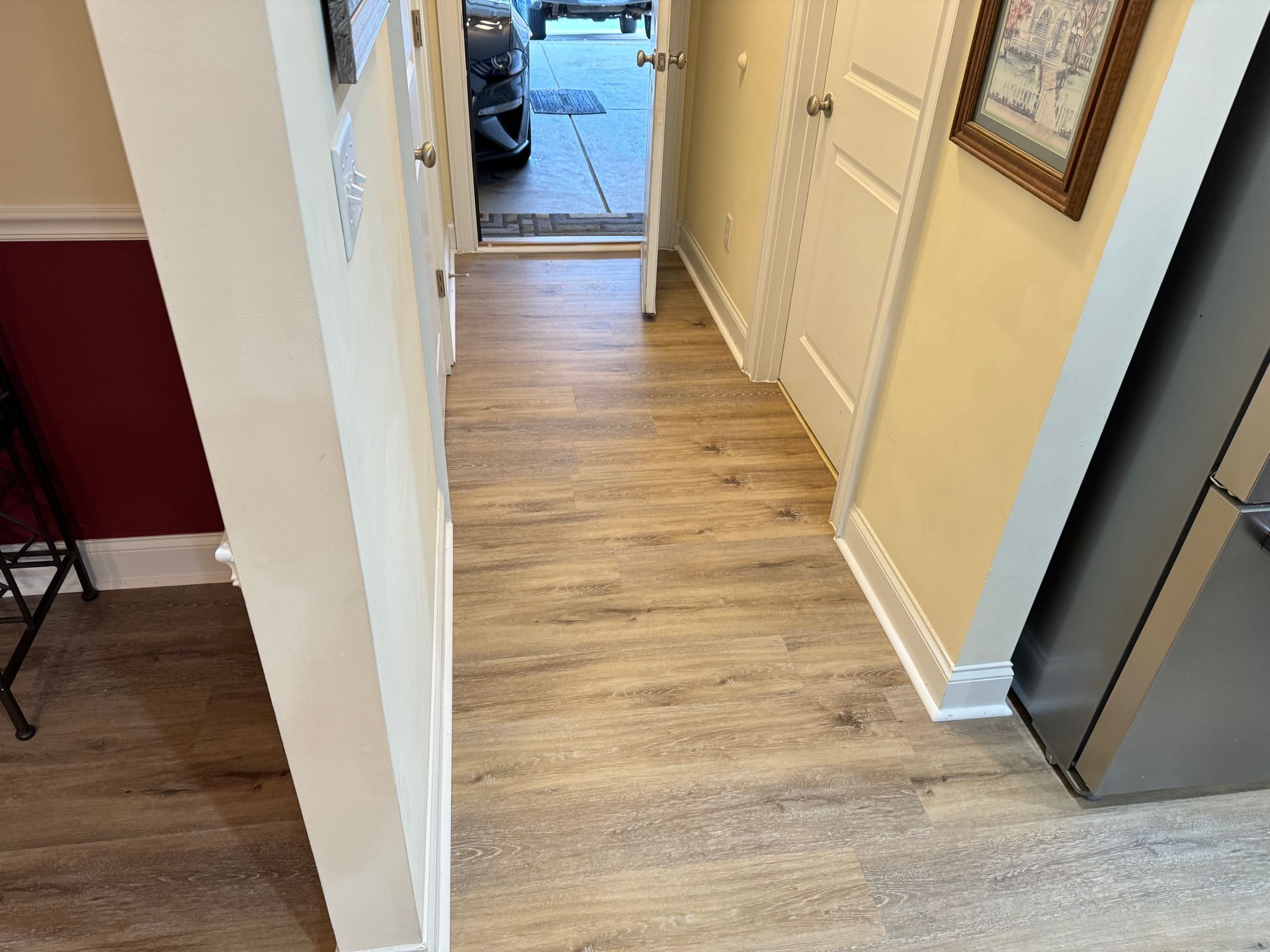 Narrow hallway with wood-look flooring, open door to outside, light-colored walls, and a red wall.