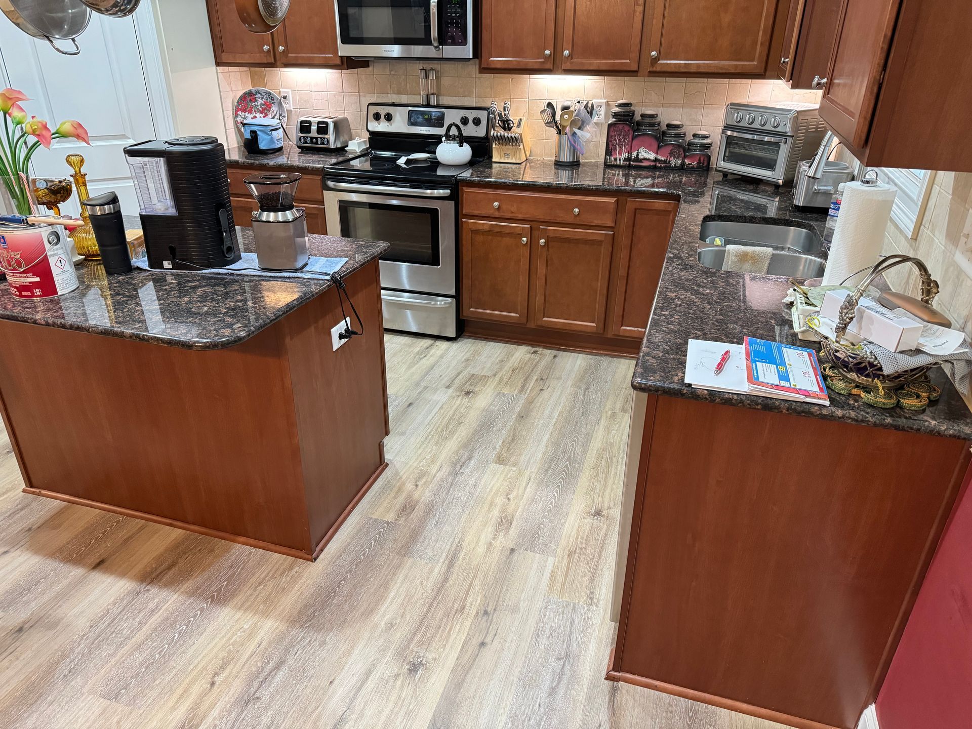 Kitchen with wood cabinets, granite countertops, stainless steel appliances, and light wood-look flooring.
