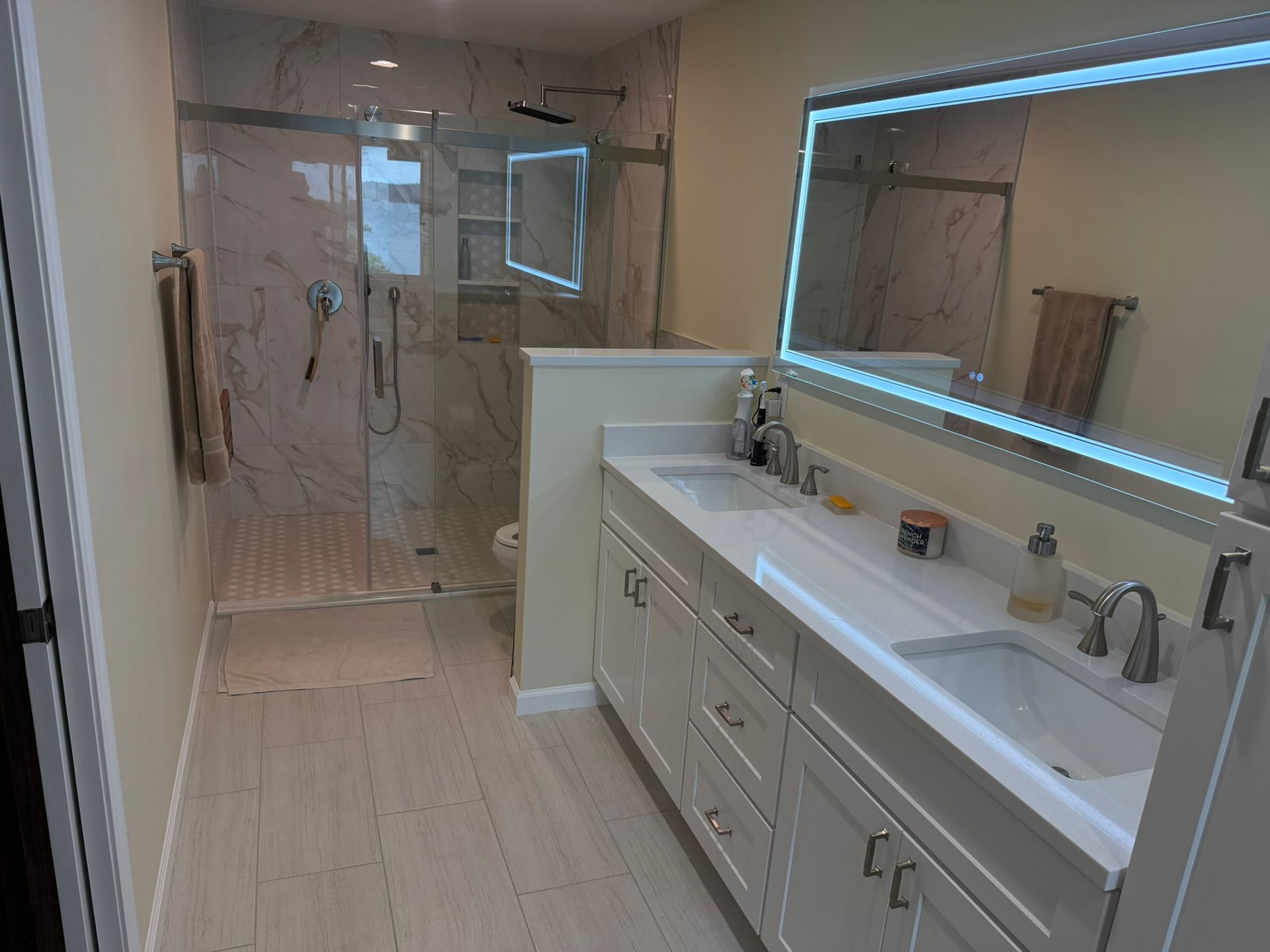Modern bathroom with double vanity, marble shower, and backlit mirror.