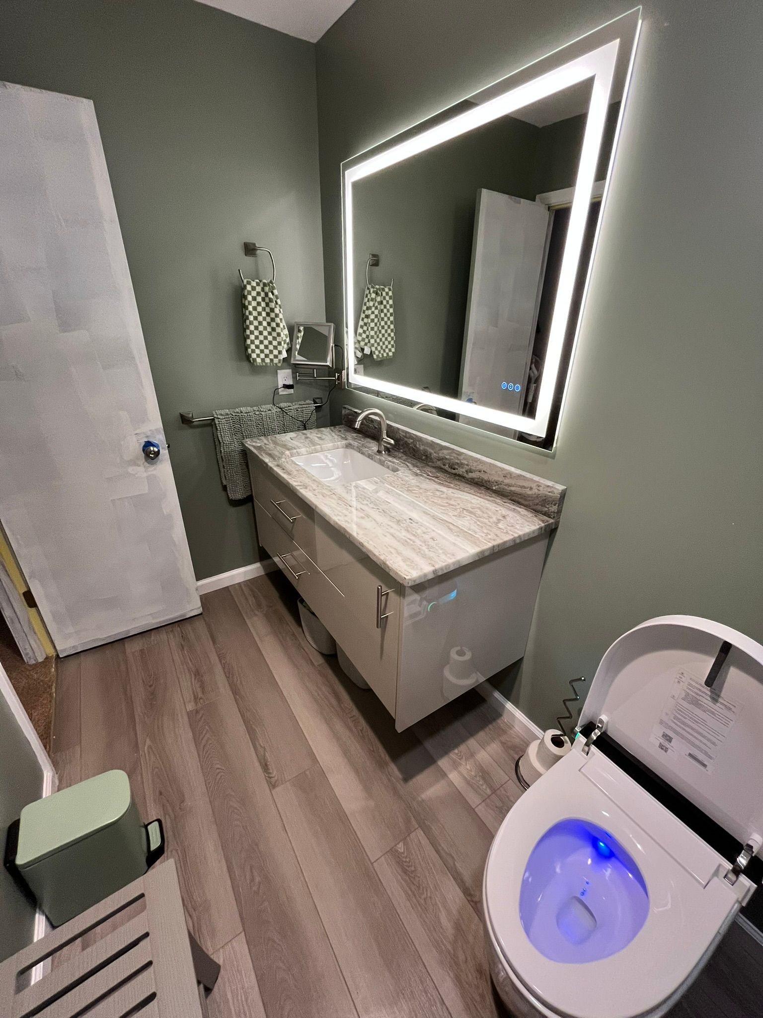Modern bathroom with floating vanity, lit mirror, bidet toilet, and sage green walls.