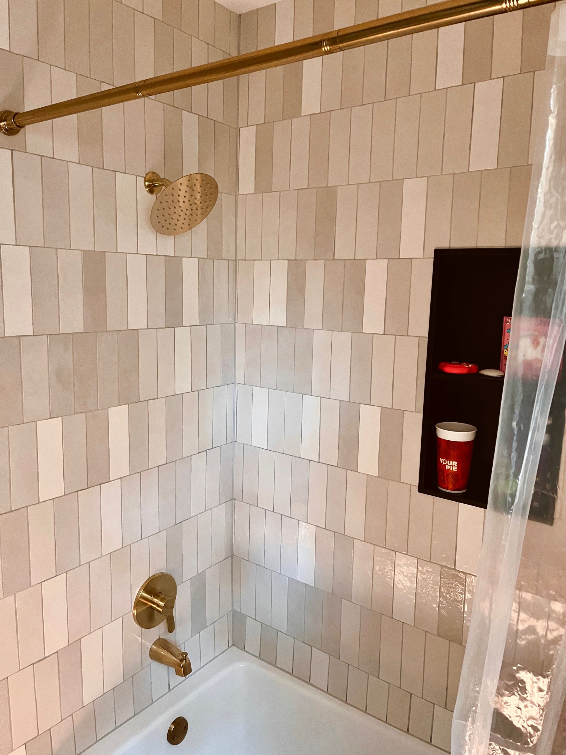 Beige and white wavy tile shower with gold fixtures, including a shower head and faucet.