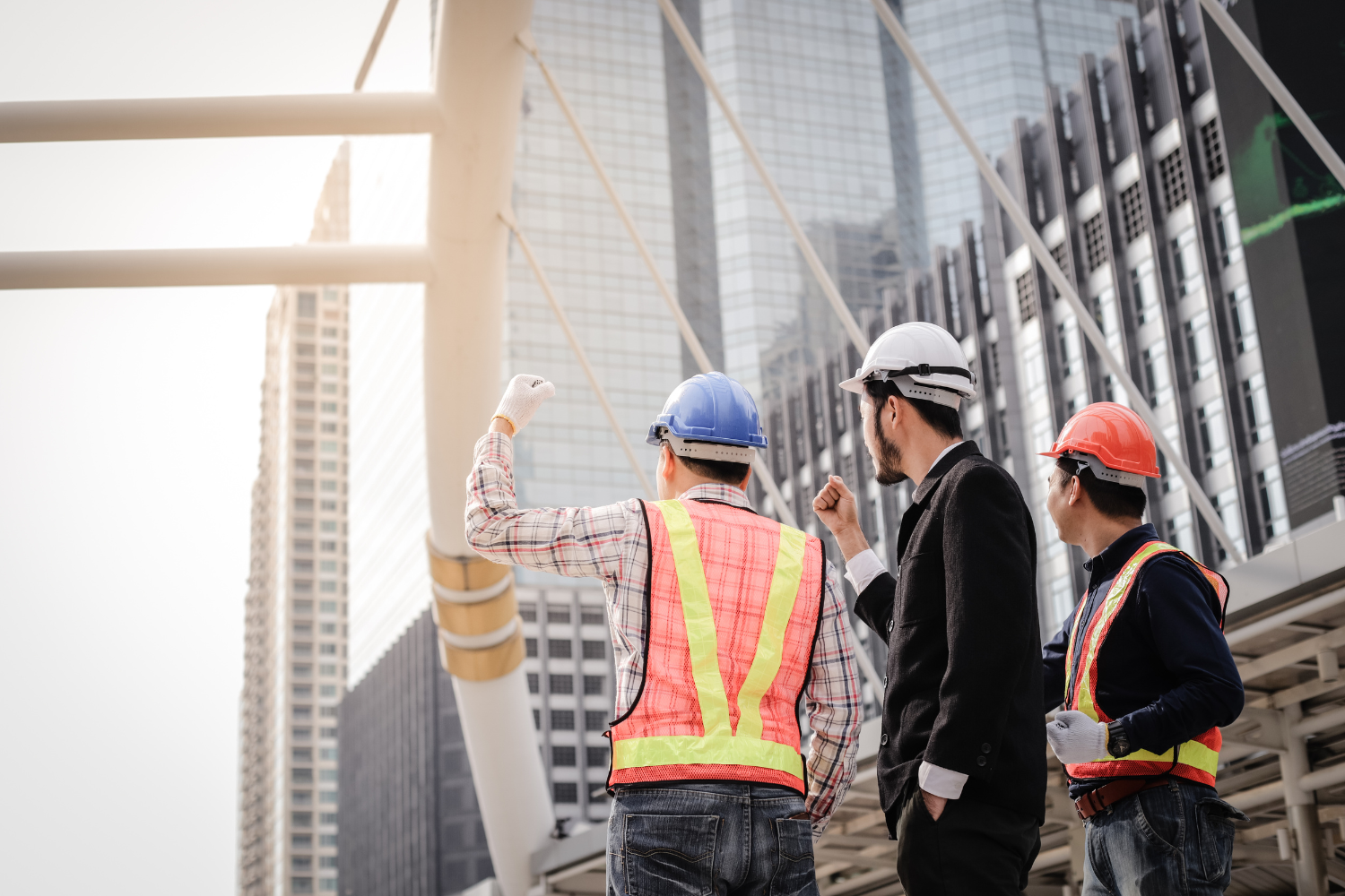 Three construction workers in hard hats looking up at skyscrapers.