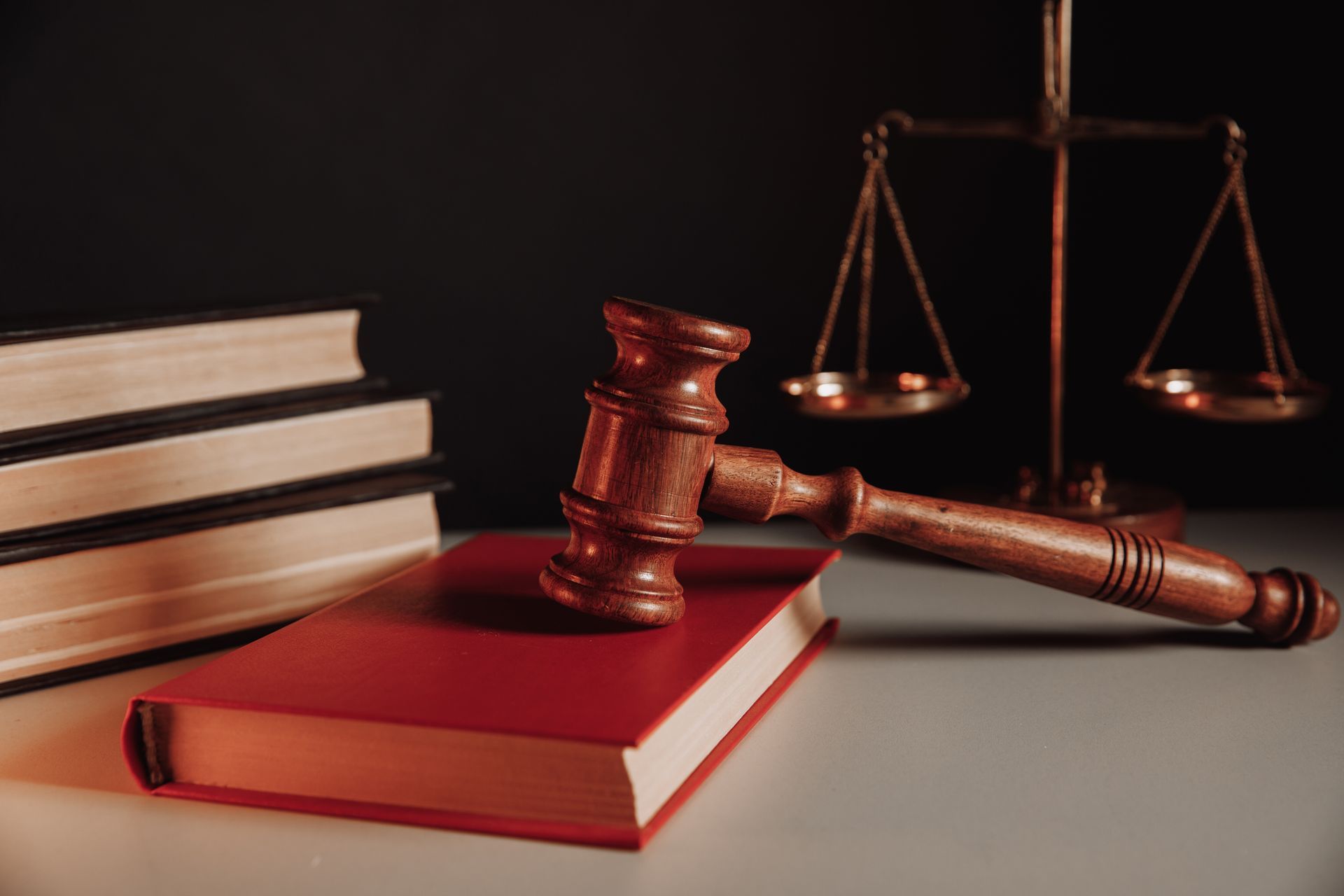 Wooden gavel resting on a red book, with law books and scales of justice in the background.