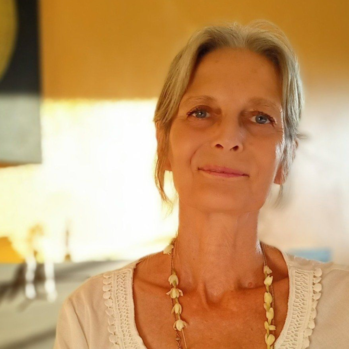 Une femme portant une chemise blanche et un collier sourit à la caméra