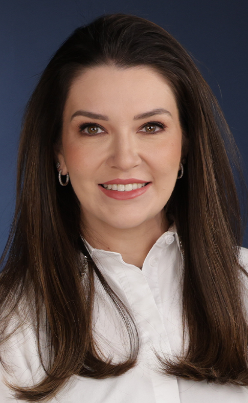 Uma mulher com longos cabelos castanhos está vestindo uma camisa branca e sorrindo.