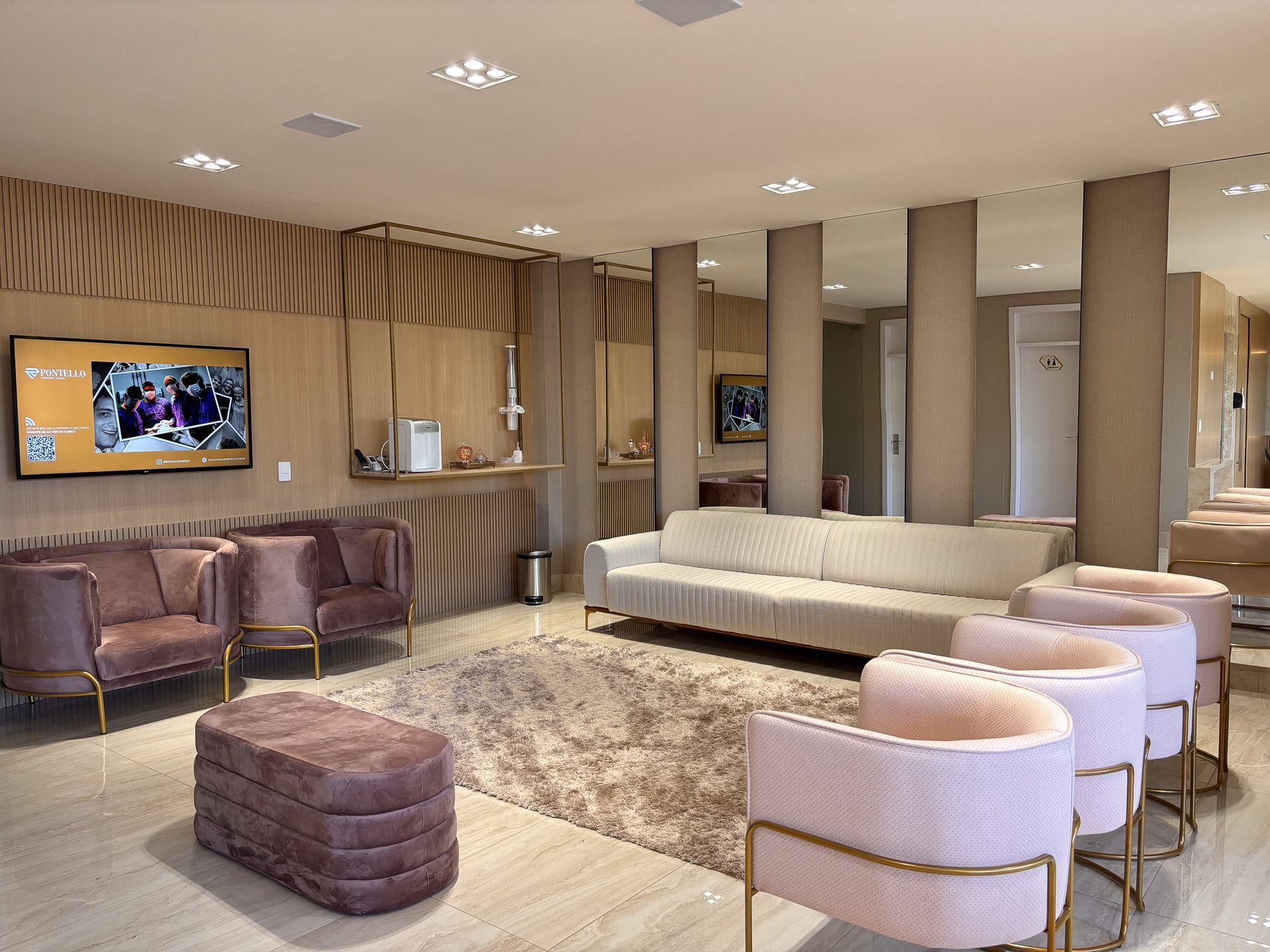 Uma sala de estar com sofá, cadeiras, pufe e televisão.