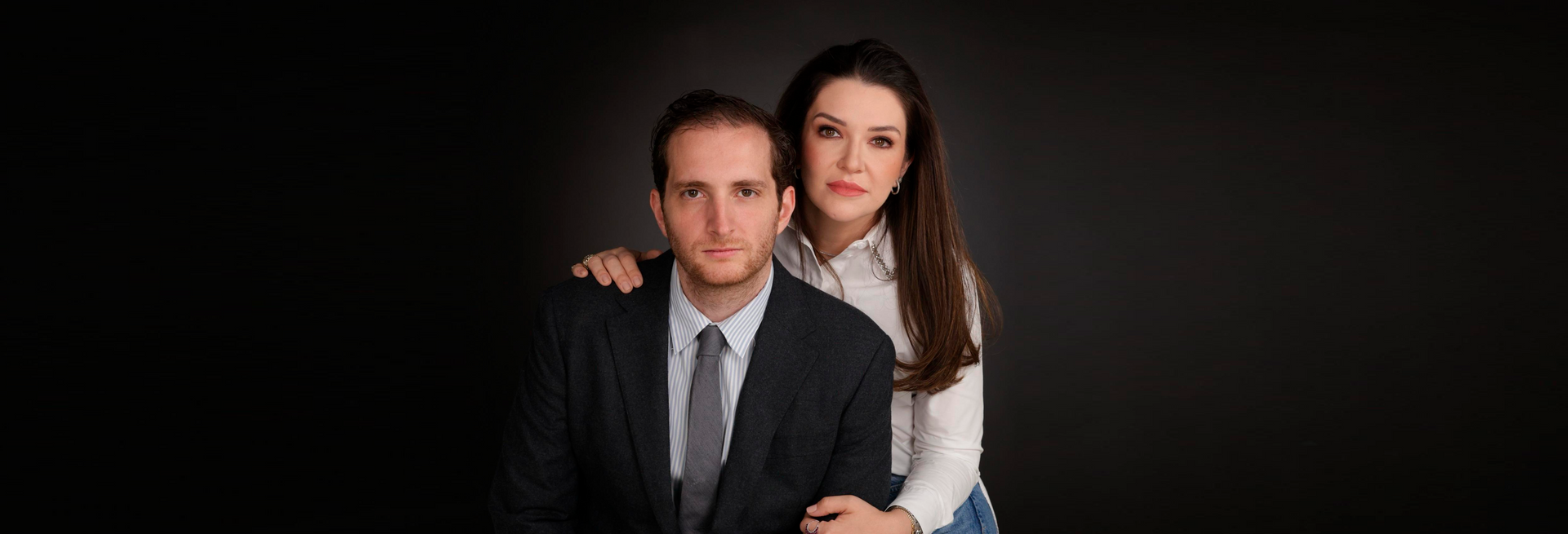 Um homem de terno e gravata está de pé ao lado de uma mulher de camisa branca.