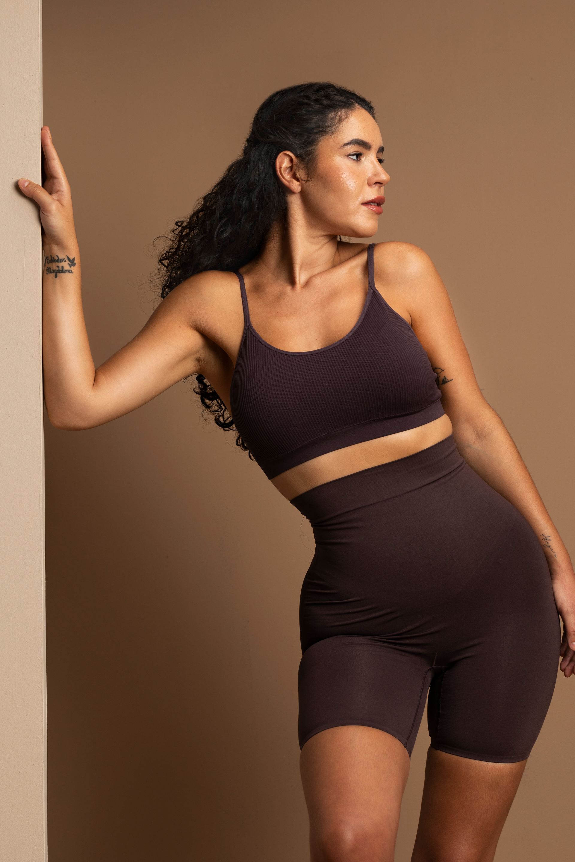 Uma mulher de top curto e shorts está encostada na parede.