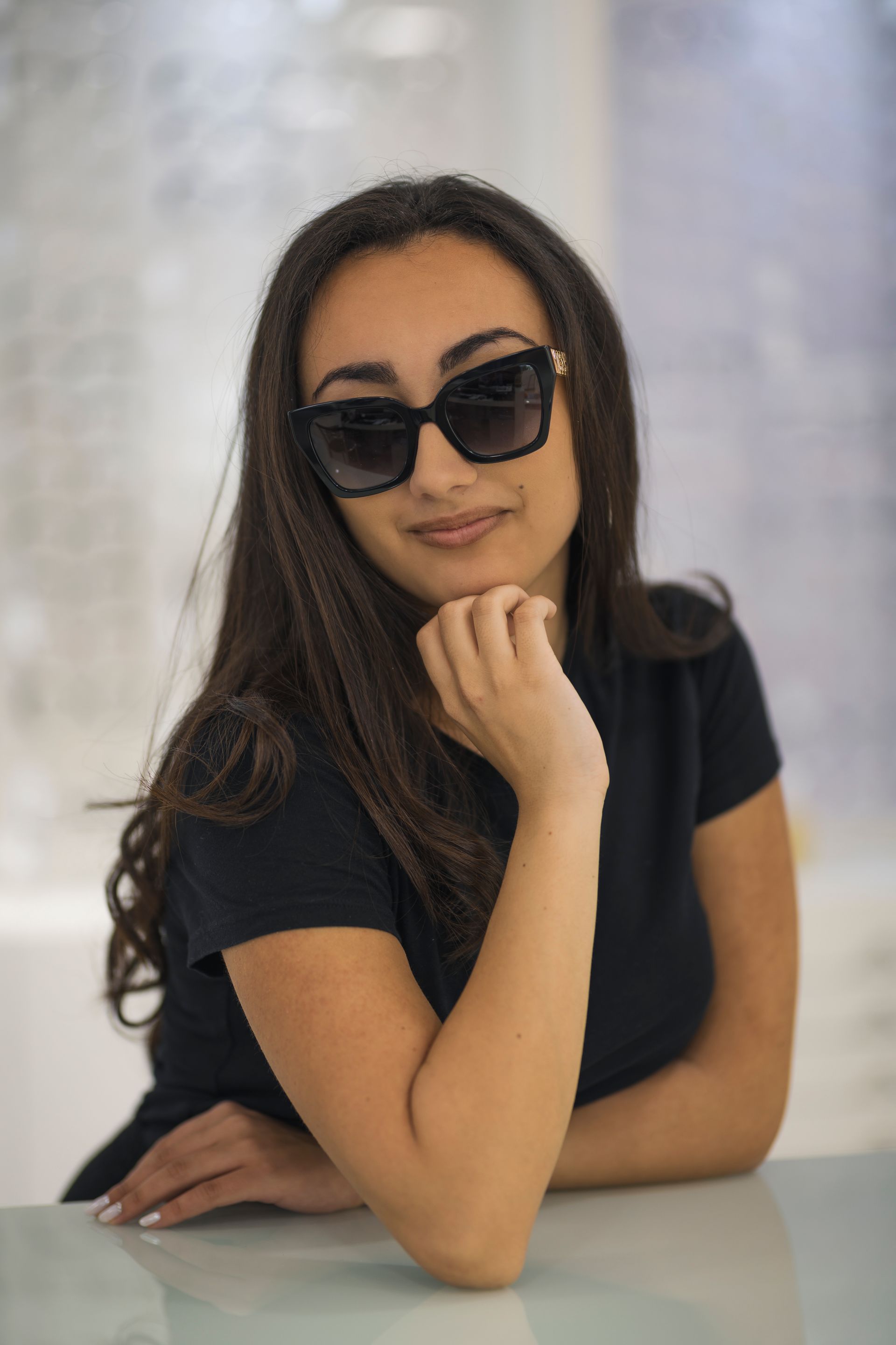 Una donna che indossa occhiali da sole e una camicia nera è seduta a un tavolo.