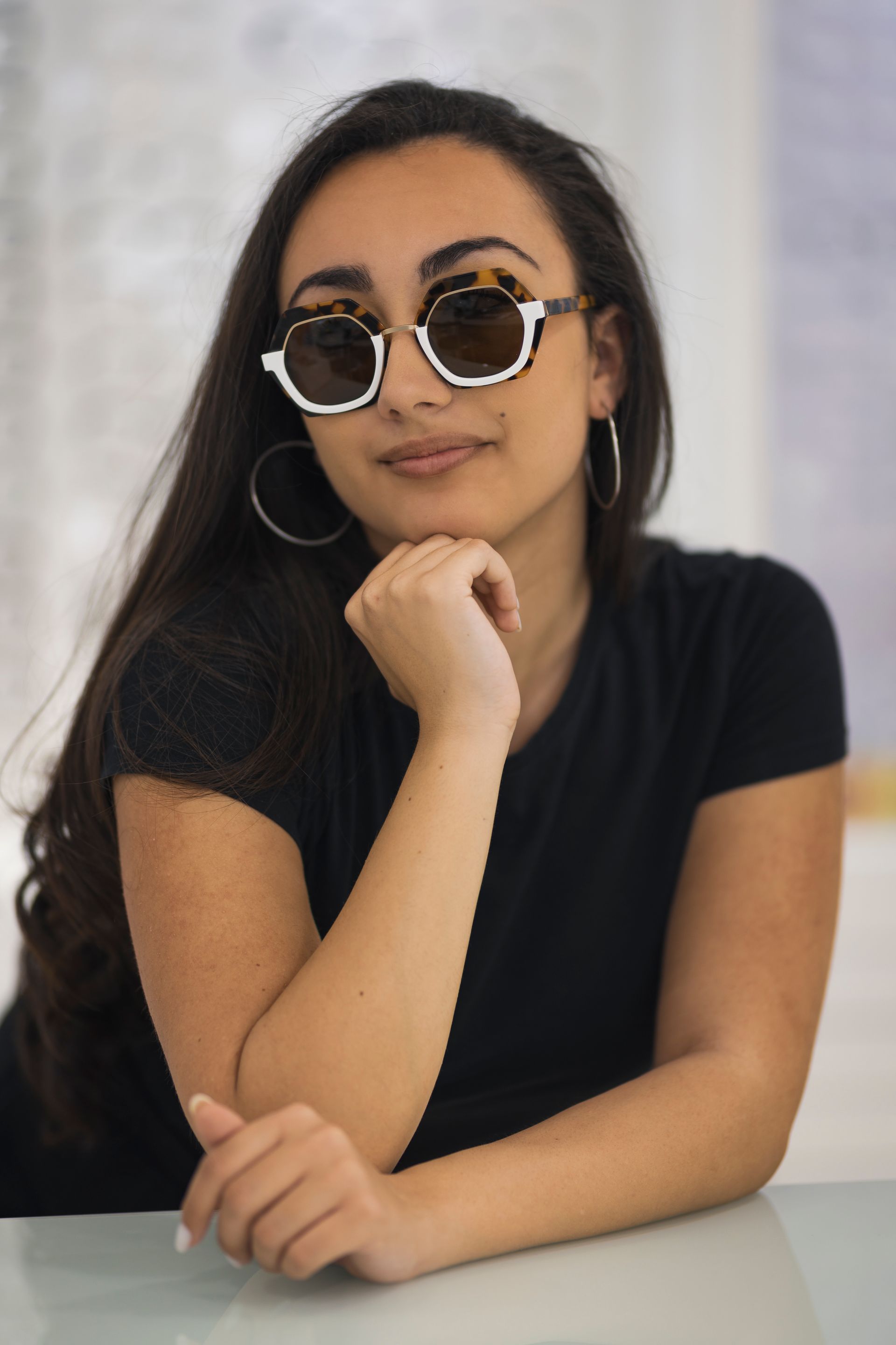 Una donna seduta a un tavolo con occhiali da sole e orecchini a cerchio.