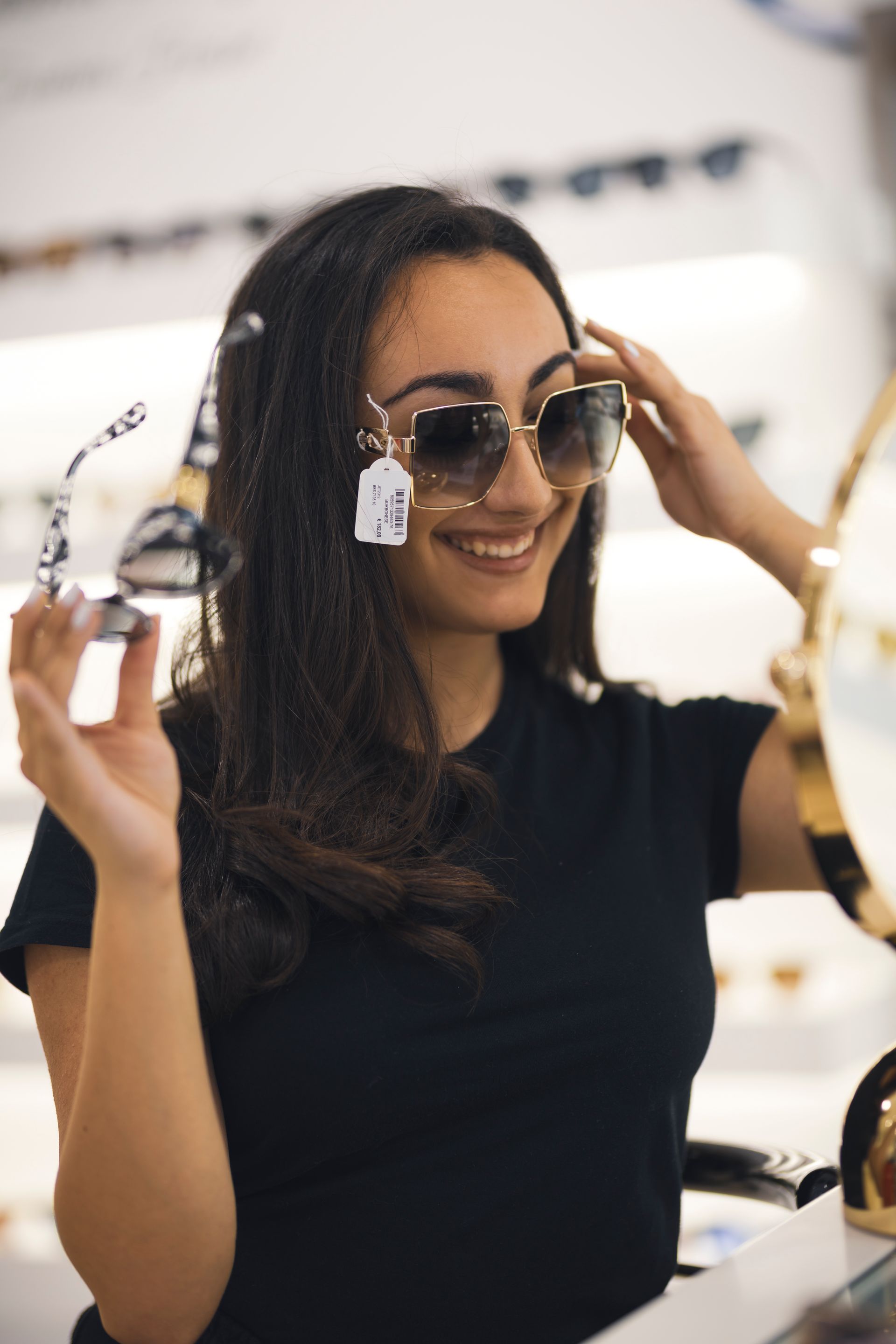 Una donna sta provando degli occhiali da sole davanti a uno specchio.