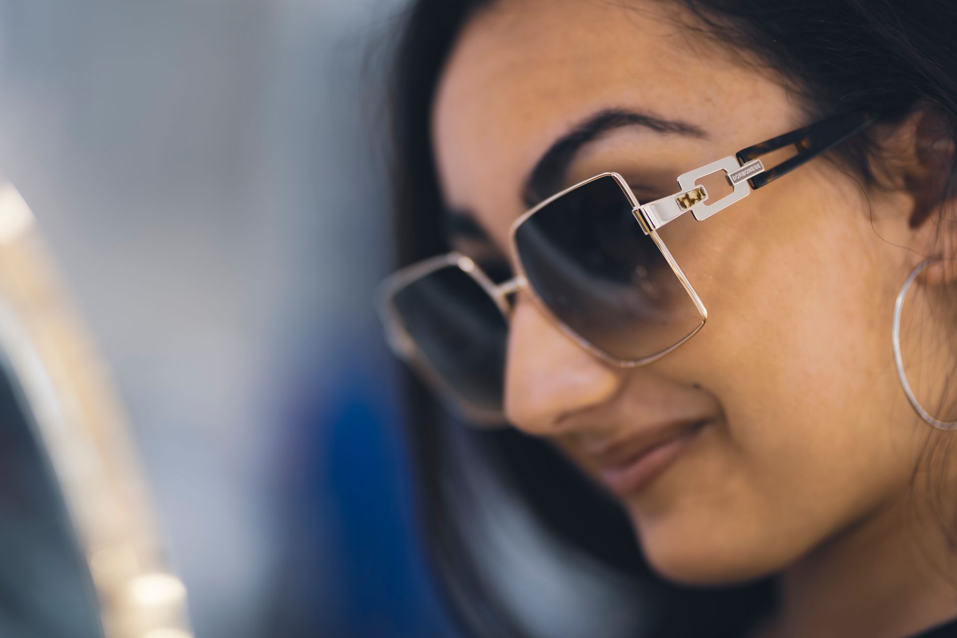 Primo piano di una donna che indossa occhiali da sole e orecchini a cerchio.